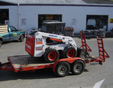 Our tandem-axle trailer, holding a skid-steer loader, being towed by a 3/4 tonne truck.