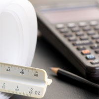 A ruler, pencil, calculator, and blueprints sitting on a desk.